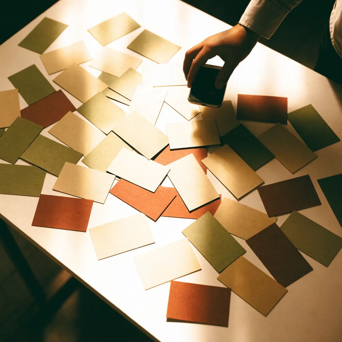 A table covered in paper business cards, one being photographed with a phone